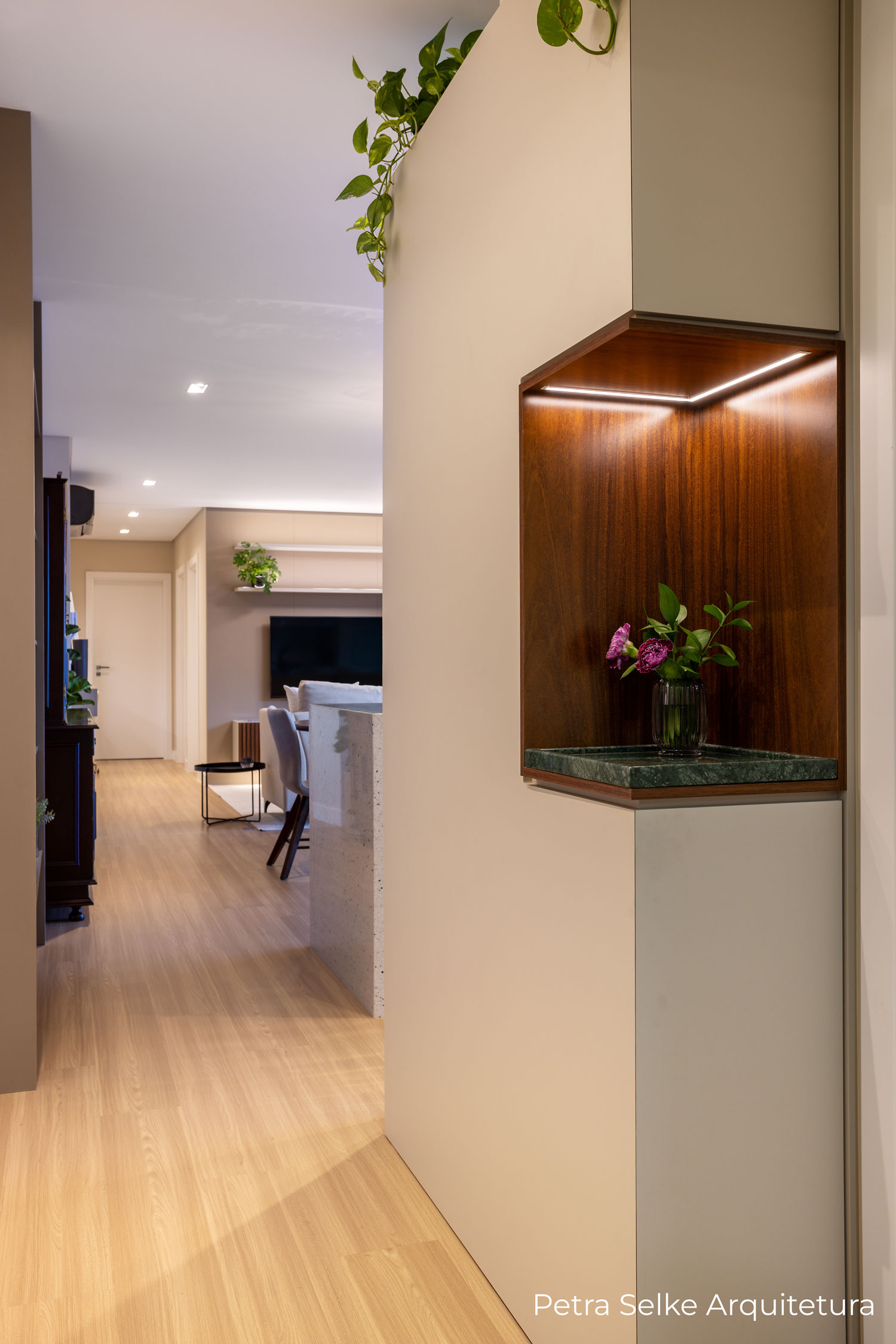 Hall de entrada moderna e minimalista com painel usinado em MDF bege, nicho em MDF madeirado escuro e bandeja em mármore Verde Alpi. Porta discreta na frente