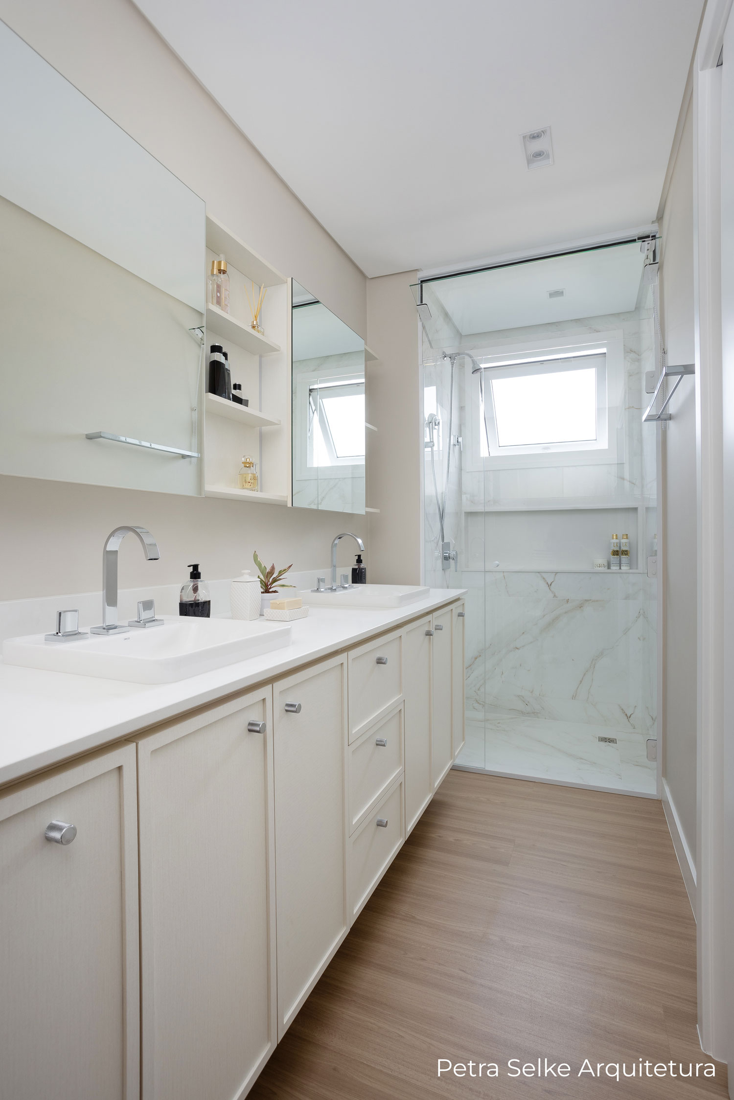 Banheiro com aéreo de portas deslizantes em espelho, balcão em MDF branco com portas e gavetas com molduras em MDF branco.